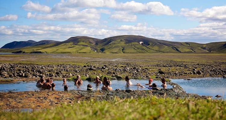 Los viajeros se relajan en una piscina de aguas termales naturales ubicada en una amplia llanura volcánica verde