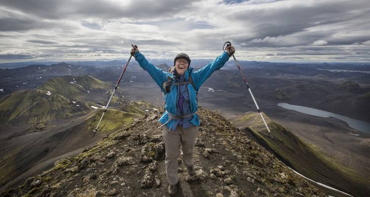 Excursionista eufórico con bastones de senderismo levantados de pie triunfante en la cima de una escarpada cresta volcánica