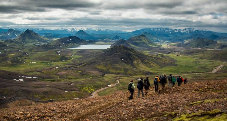 Hikers descending a trail with expansive views of green mountains and lakes.