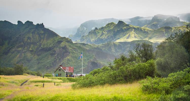 House with red roof in a lush valley with rugged mountains in the distance.