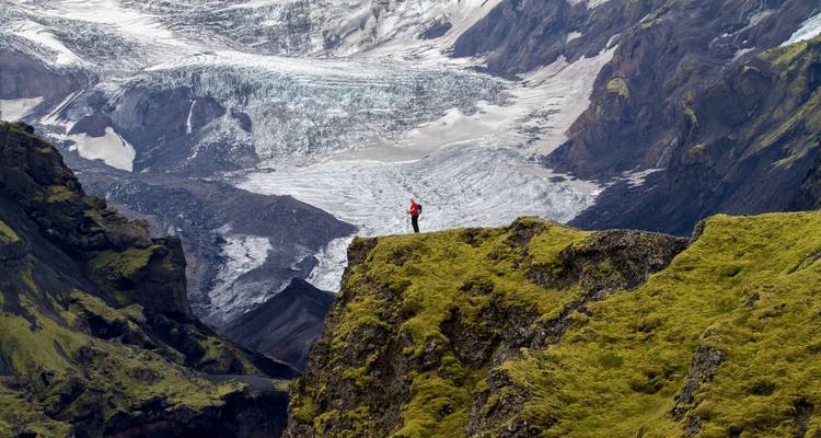 Person standing on a rocky cliff overlooking a glacier and mountains.
