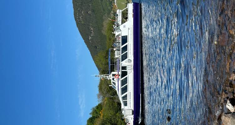 El barco de pasajeros "Jacobite Warrior" está amarrado en el tranquilo Loch Ness con colinas boscosas detrás.