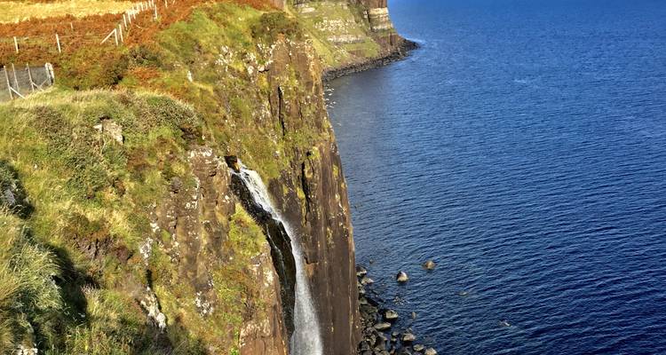 Een smal waterval stort zich neer over mosachtige rotsen in de diepblauwe zee naast Kilt Rock.