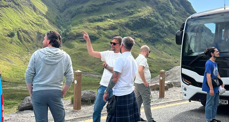 Un petit groupe discute à côté d'un autocar de tourisme garé dans une vallée montagnarde verdoyante.