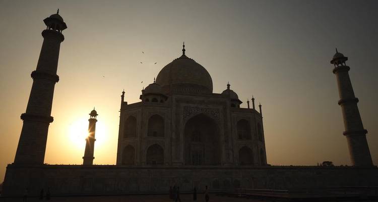Silhouette of the Taj Mahal against a golden sunrise with birds flying overhead