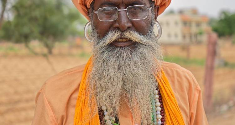 Close portrait of bearded sadhu in orange robe and turban wearing glasses and beads