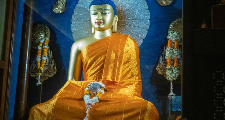 Statue de Bouddha dorée d'intérieur drapée de robes orange avec un arrière-plan orné.