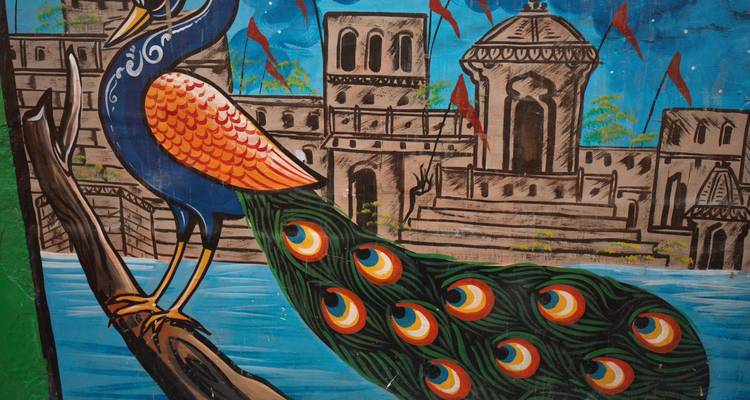 Colourful wall painting of a peacock and historic architecture on a vibrant blue background