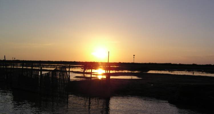 Puesta de sol sobre una masa de agua con estructuras silueteadas.