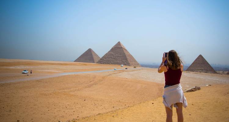 Eine weibliche Reisende fotografiert die Pyramiden von Giza aus der umgebenden Wüstenlandschaft.