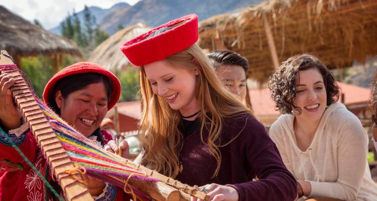 Visitors enjoy hands-on weaving with bright wool threads in a sunny Andean craft village.