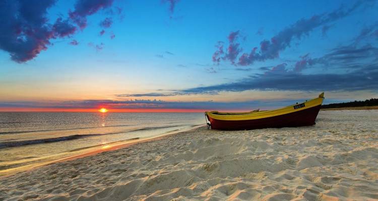 Barco de colores en una playa de arena durante una serena puesta de sol.