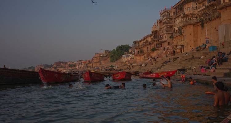 Locals swimming in the Ganges beside red boats and stone ghats at dusk
