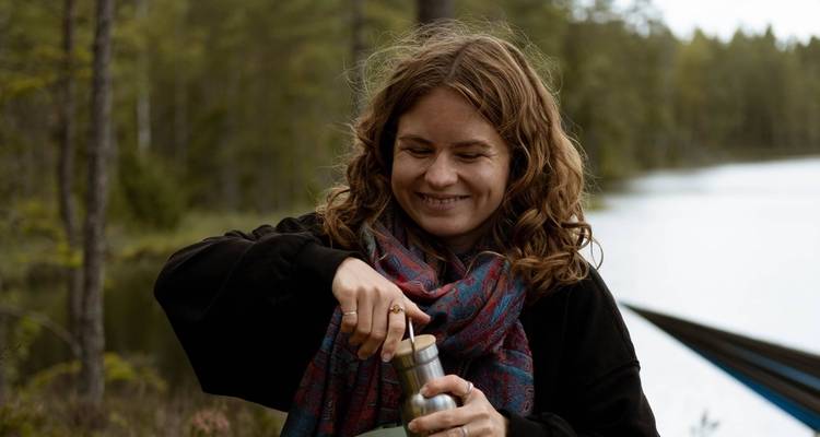 Woman preparing a drink by a lake in a forest.