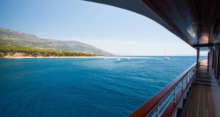 Vue depuis le pont d'un yacht surplombant la mer avec des voiliers et une côte.