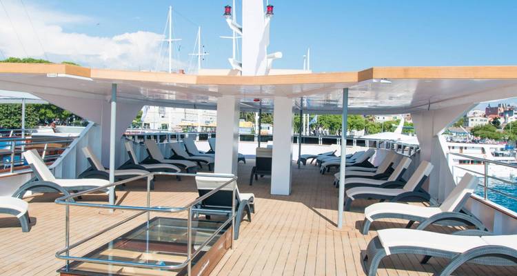 Pont ensoleillé d'un yacht avec plusieurs chaises longues et vue sur la ville.