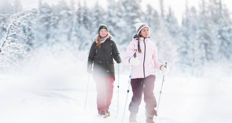 Dos mujeres caminando con bastones de senderismo en un bosque nevado.
