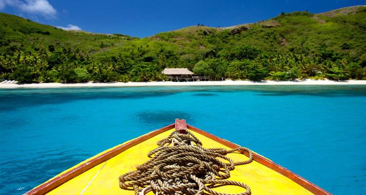 L'avant d'un bateau jaune pointe vers une île aux sables blancs de l'autre côté d'une eau turquoise éclatante sous un ciel dégagé.