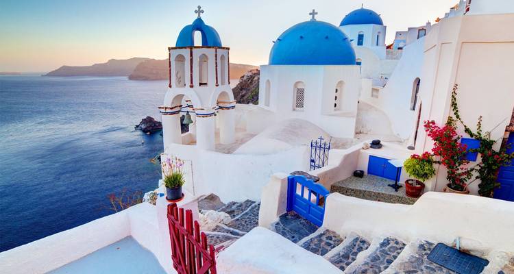 Les églises emblématiques aux dômes bleus et les maisons blanchies à la chaux d'Oia s'étagent le long des falaises dominant la mer Égée au coucher du soleil.