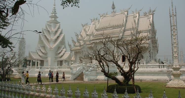 Temple blanc avec des motifs complexes et des arbres, des gens marchant autour.