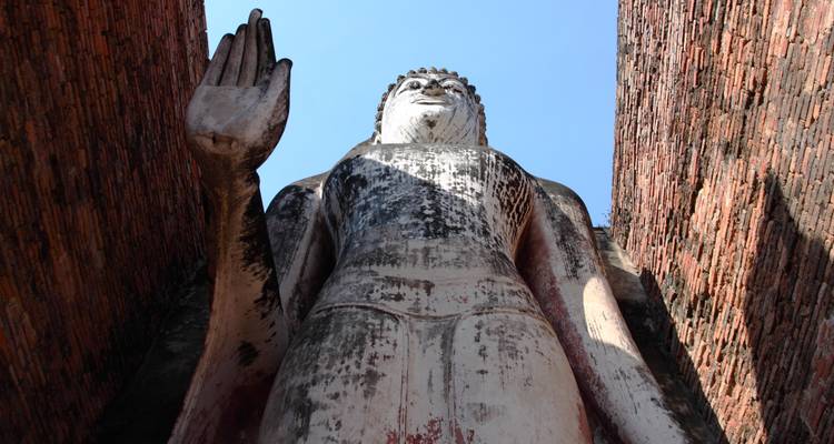 Große stehende Buddha-Statue zwischen Backsteinmauern.