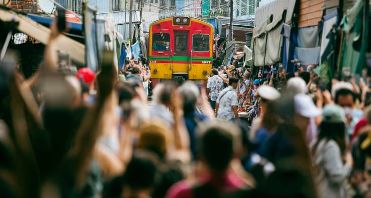 Un train rouge vif et jaune circule dans une rue de marché bondée avec des personnes photographiant à quelques centimètres de distance
