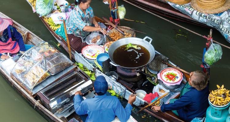 Vue aérienne de bateaux en bois colorés à un marché flottant, des vendeurs cuisinant et vendant des aliments sur un canal étroit.