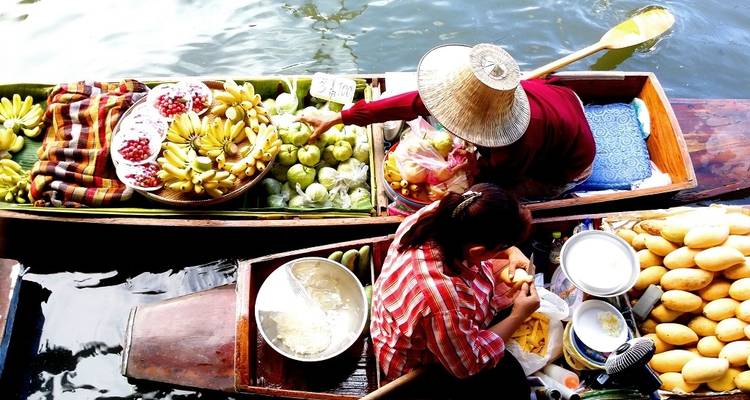Deux vendeurs arrangeant des fruits sur des bateaux dans un marché flottant.