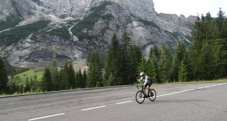 Ciclista en una carretera con grandes montañas rocosas en el fondo.
