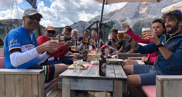 Grupo de personas brindando con cerveza en un patio con montañas.