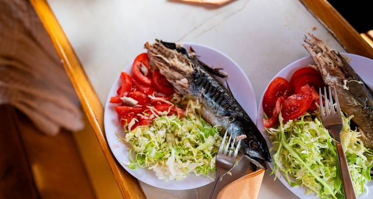 Assiettes de poisson grillé servies avec de la laitue râpée et des tomates fraîches sur une table de bateau.