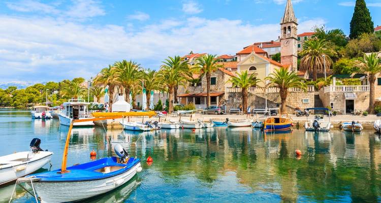 A picturesque Croatian coastal village with palm trees and small boats moored in crystalline water.
