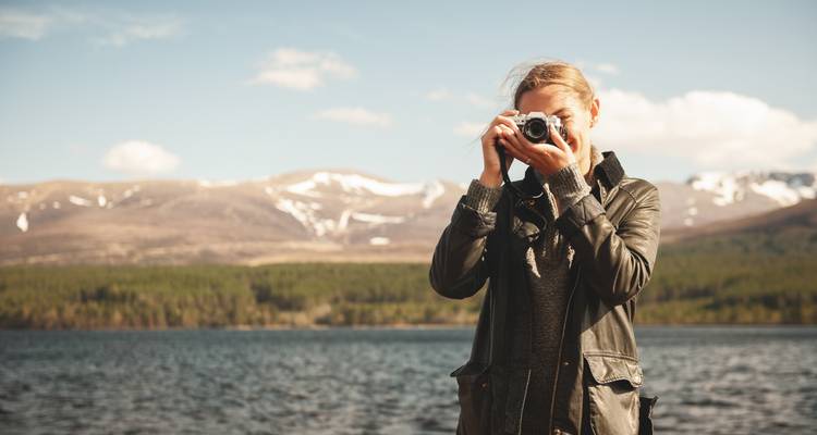 Una persona tomando una foto con montañas y un lago de fondo.
