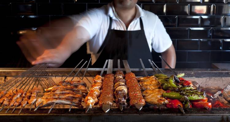 Chef grilling skewers of various meats and vegetables on a barbecue.