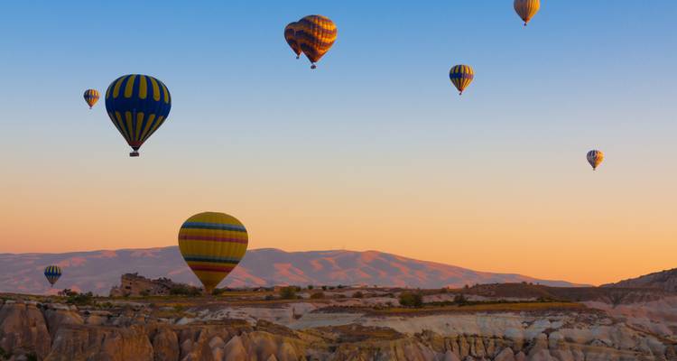 Hot air balloons floating over the Cappadocia landscape at sunrise.