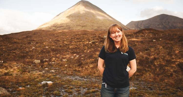 Mujer sonriendo con un paisaje montañoso detrás.
