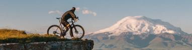 A man riding a bicycle near a cliff with a snowy mountain in the background