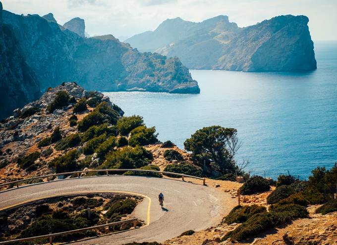 Aerial view of a cyclist riding on a road next to a blue lake