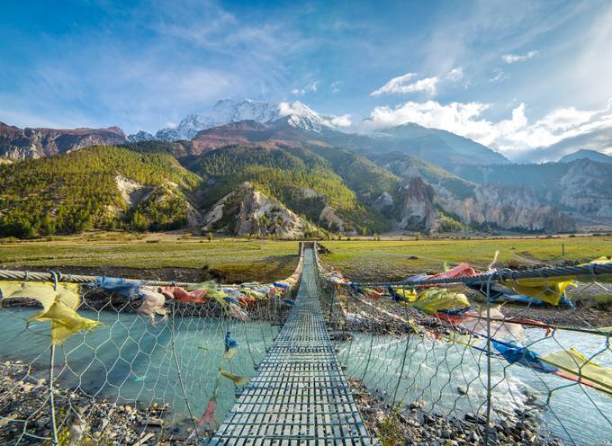 View of the Annapurna Mountains from a bridge covered in Buddhist flags in Nepal