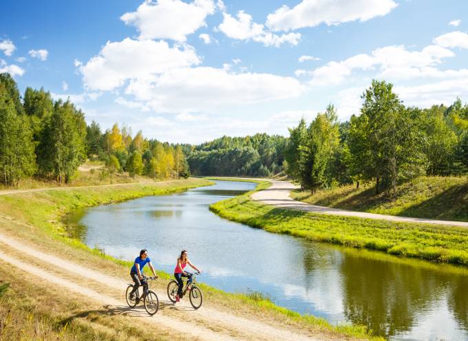 Two cyclists riding together next to a flowing river