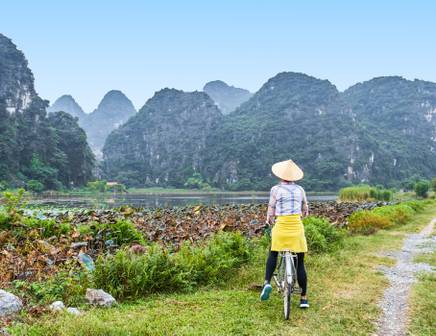 A woman on a yellow bicycle gazing at the limestone peaks of Vietnam