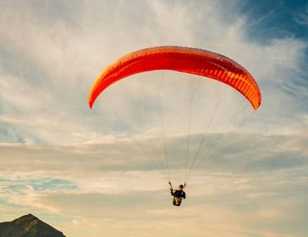 A man with a red paraglider floating high above the mountains of New Zealand