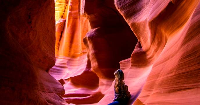 A woman gazing up through the colourful sunlit cracks of Antelope Canyon, USA