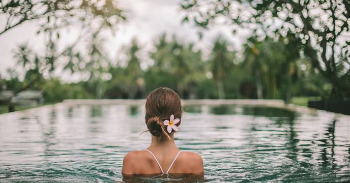 A woman facing away witha. frangipani in her hair relaxing in a hotel pool