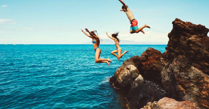A group of friends having fun as they jump off a cliff into the ocean below