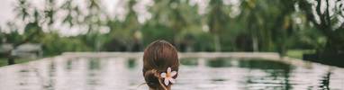 Woman in an infinity pool relaxing with a frangipani in her hair