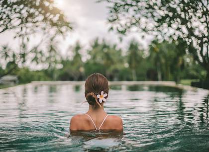 Woman in an infinity pool relaxing with a frangipani in her hair