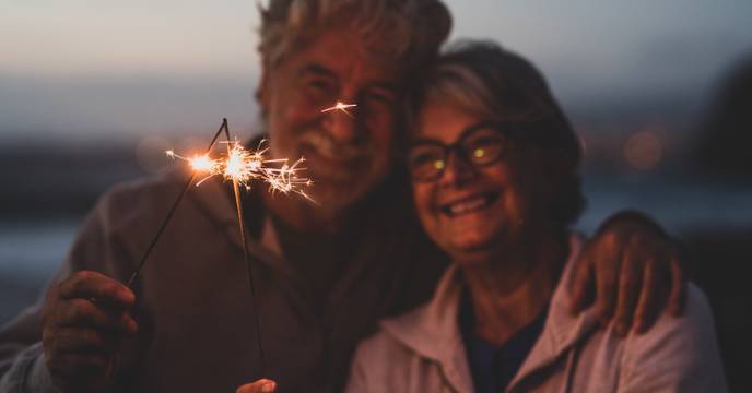 An elderly couple cuddling up to each other whilst celebrating with sparklers, or fireworks together