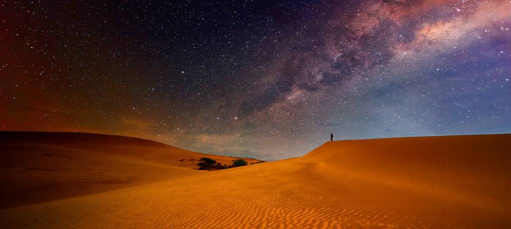 Reisender auf einem Abenteuer in den Dünen der Sahara blickt in den Sternenhimmel