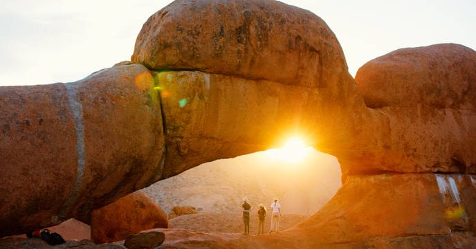 Drei Reisende sonnen sich unter dem Natural Arch in Damaraland, Skelettküste